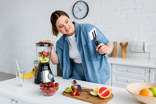 cheerful plus size Vlog using smartphone while preparing smoothie in kitchen