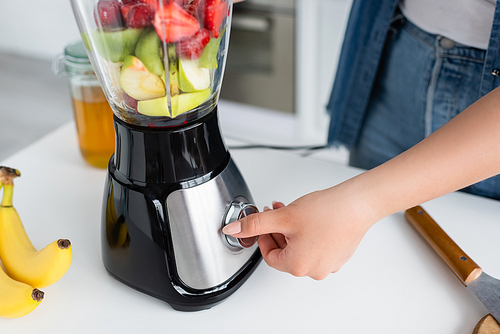 Cropped view of plus size woman switching blender while cooking smoothie in kitchen