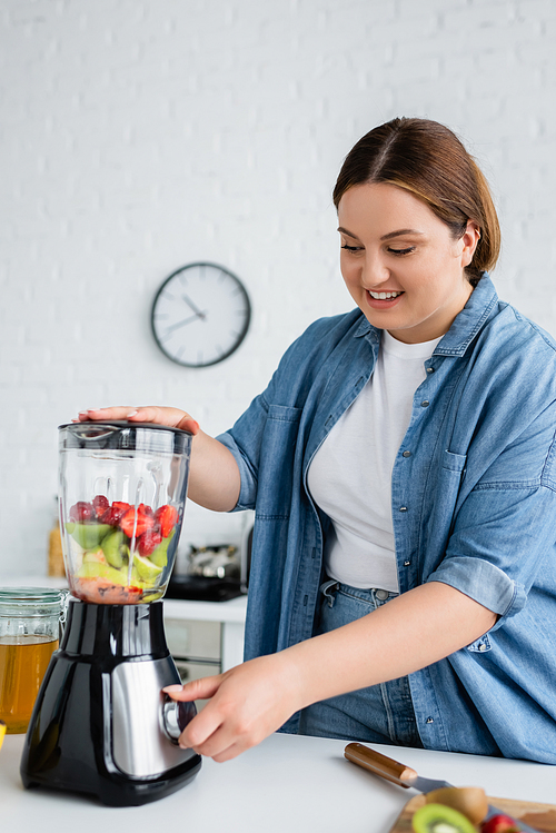Cheerful woman with overweight making smoothie near honey in kitchen
