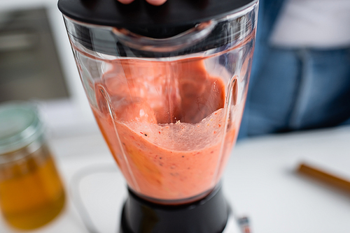 Cropped view of smoothie in blender near blurred woman in kitchen