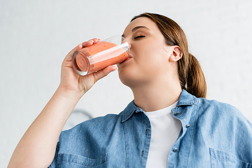 Low angle view of young woman with overweight drinking smoothie at home