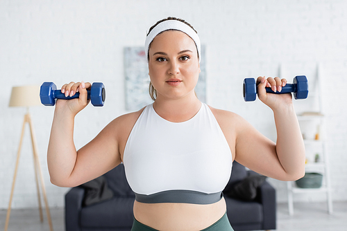 Young woman with overweight exercising with dumbbells and  at home