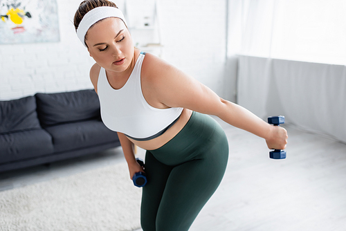 Plus size sportswoman working out with dumbbells in living room