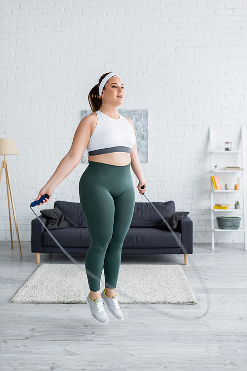 Young plus size woman jumping with skipping rope in living room
