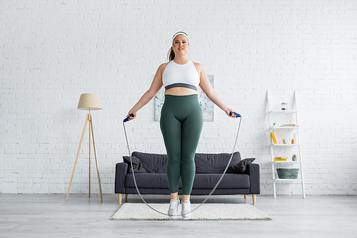 Smiling plus size woman training with skipping rope in living room