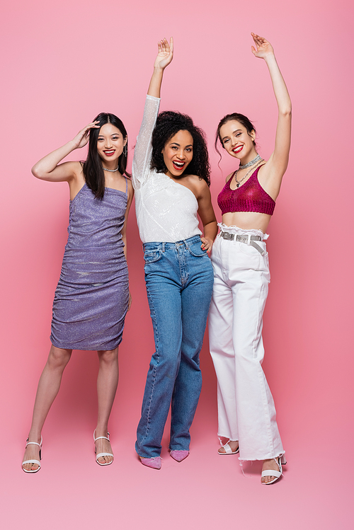 Full length of cheerful multicultural women  on pink background
