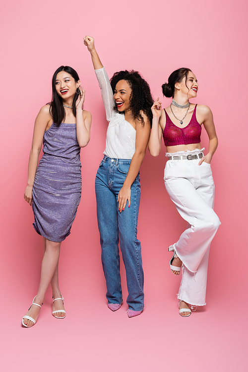 Full length of happy multicultural women posing during party on pink background