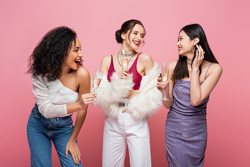Smiling multiethnic women holding glasses of champagne isolated on pink