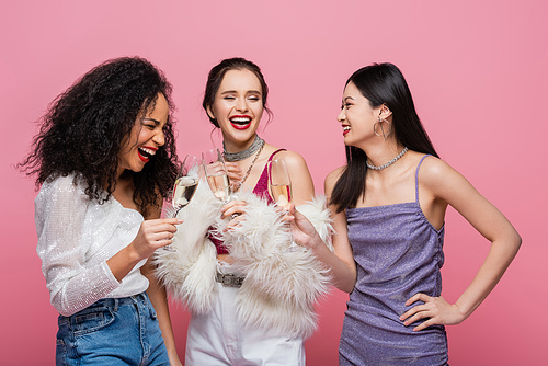 Laughing multicultural friends holding champagne during party isolated on pink