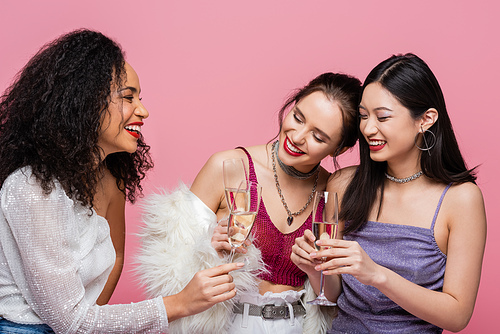 Pretty african american woman holding champagne near smiling interracial friends isolated on pink