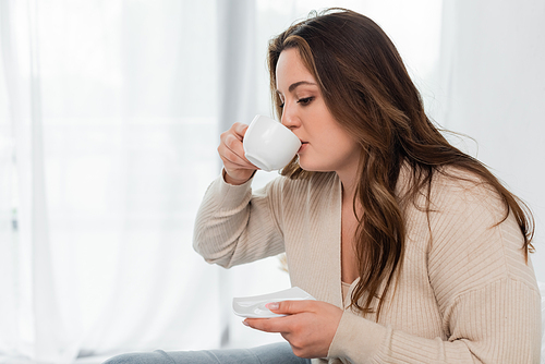 Pretty plus size woman drinking coffee at home