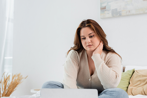 Young freelancer with overweight looking at blurred laptop at home