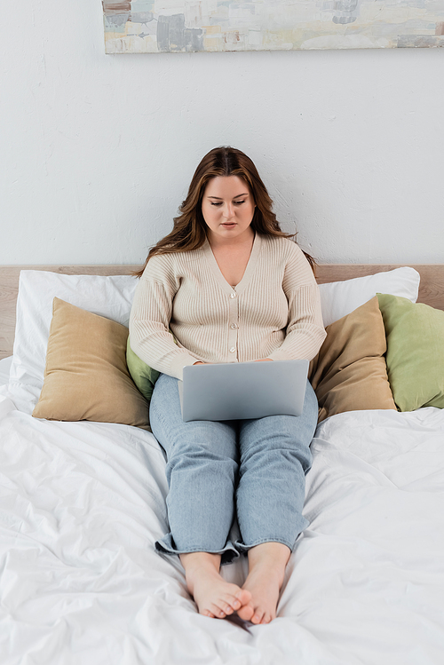 Pretty body positive woman working on laptop on bed at home