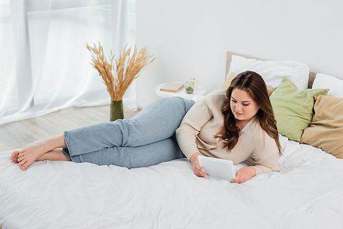 Barefoot plus size woman using digital tablet on bed