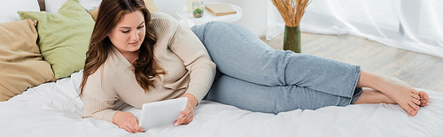 Young woman with overweight using digital tablet while lying on bed, banner