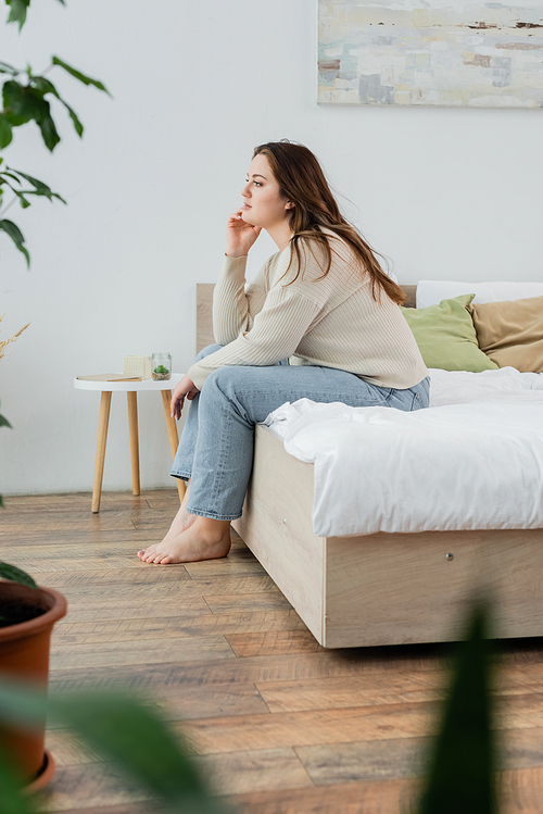 Side view of young body positive woman sitting on bed at home