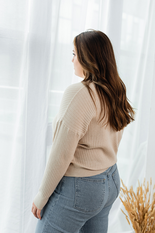 Young plus size woman standing near curtains at home