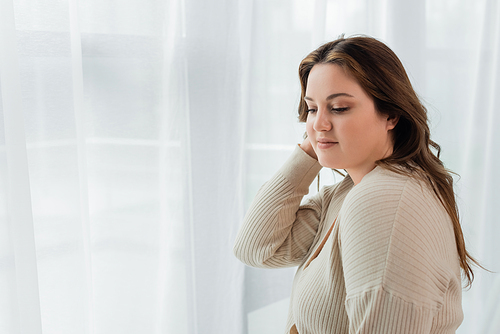 Pretty body positive woman standing near curtains at home