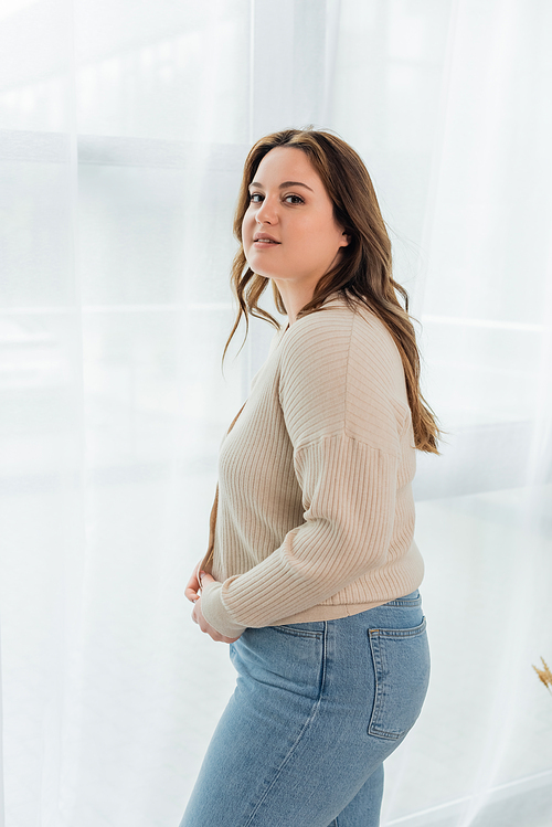 Smiling body positive woman in casual clothes  near curtains at home