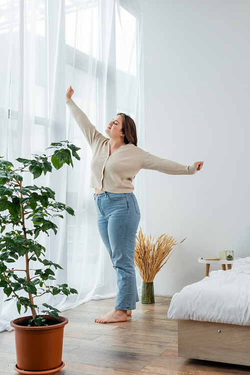 Young body positive woman stretching near window in bedroom