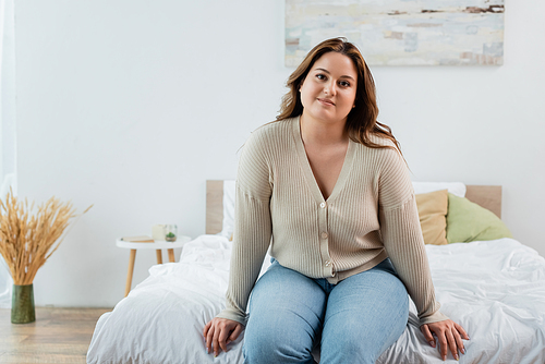 Smiling woman with overweight sitting on bed at home