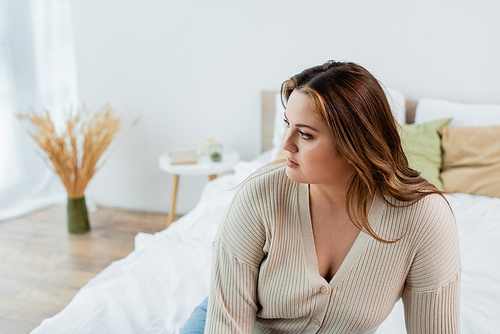 Young woman with overweight looking away on blurred bed at home