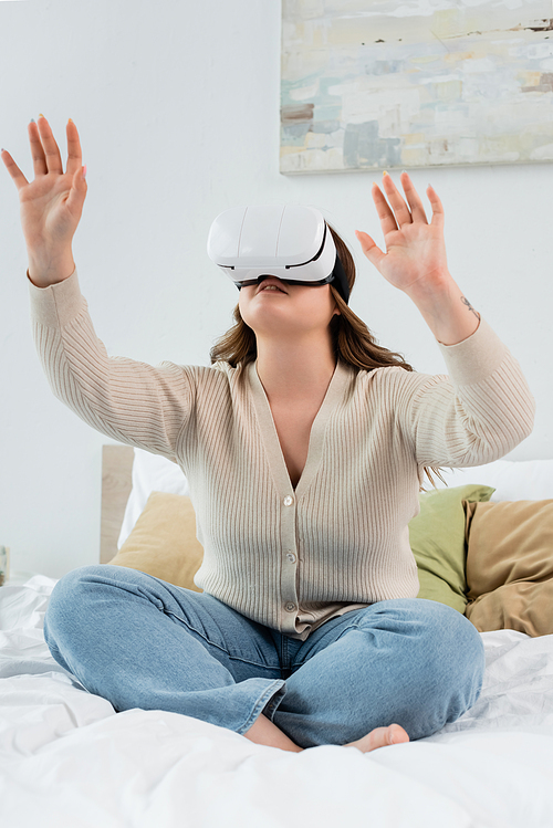 Young body positive woman gaming in vr headset while sitting on bed