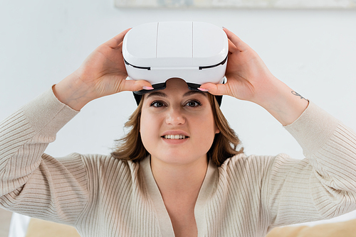 Young plus size woman smiling at camera and holding vr headset at home