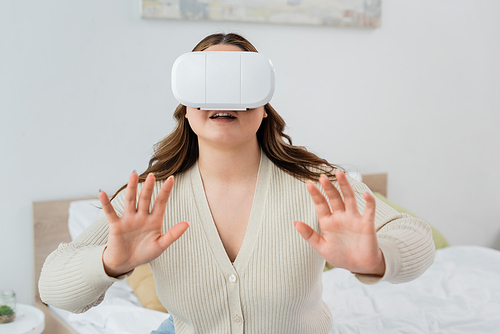 Smiling woman with overweight gaming in virtual reality headset in bedroom