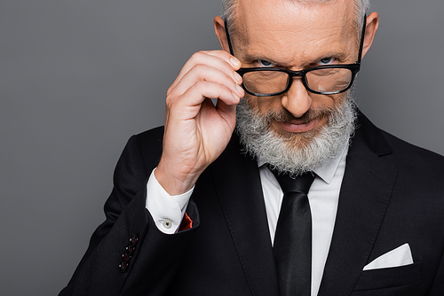 serious middle aged businessman adjusting glasses while  isolated on grey