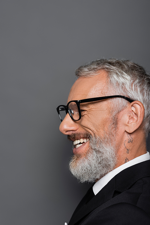 tattooed middle aged businessman in glasses smiling on grey