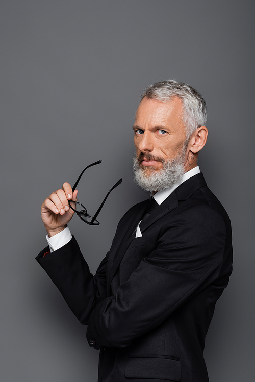 middle aged businessman in suit holding glasses on grey