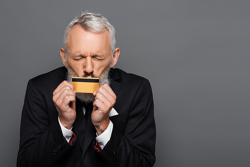 mature businessman in suit kissing credit card isolated on grey