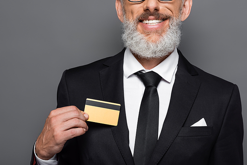 cropped view of cheerful middle aged businessman in suit holding credit card isolated on grey