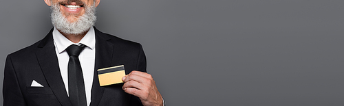 cropped view of cheerful middle aged businessman in suit holding credit card isolated on grey, banner