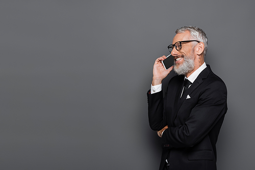 cheerful middle aged businessman talking on cellphone on grey