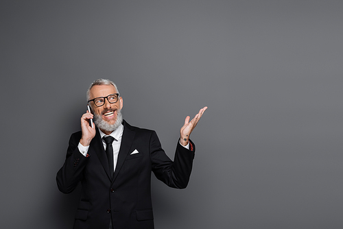 cheerful middle aged businessman talking on cellphone and gesturing on grey