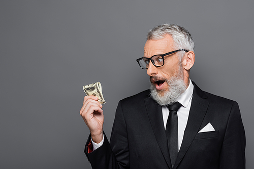 shocked middle aged businessman looking at dollar banknotes isolated on grey