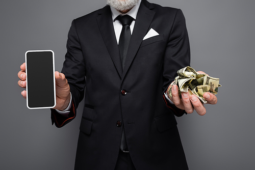 cropped view of middle aged businessman holding dollar banknotes and smartphone with blank screen isolated on grey