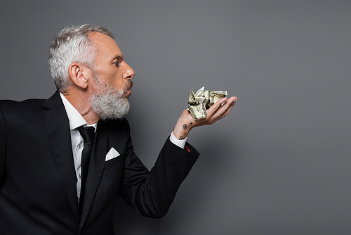 side view of tattooed middle aged businessman blowing on crumpled dollar banknotes on grey