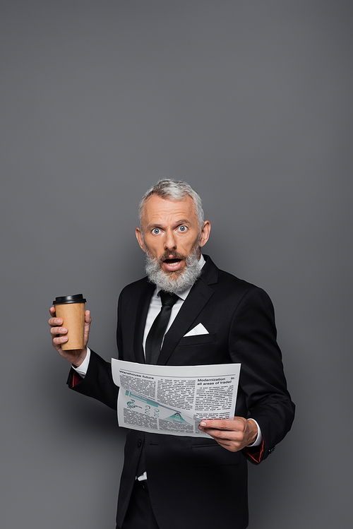 shocked middle aged businessman holding paper cup and newspaper on grey