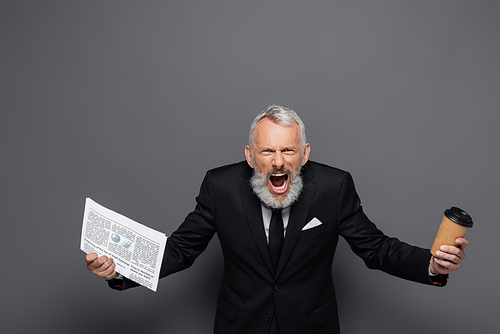 angry middle aged businessman holding paper cup and newspaper while screaming on grey