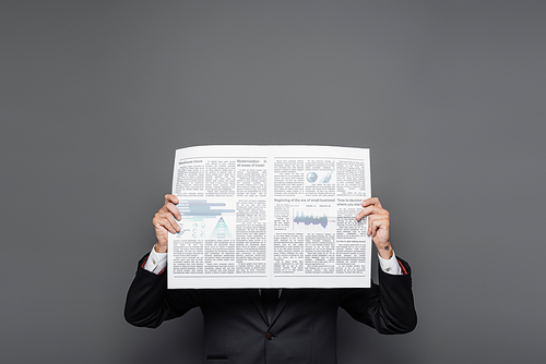 middle aged businessman obscuring face with newspaper on grey