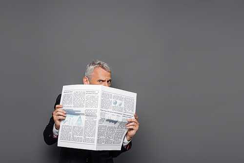 middle aged businessman covering face with newspaper on grey