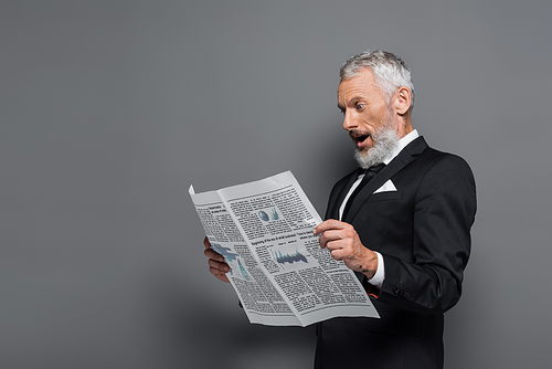 shocked middle aged man in suit reading newspaper on grey