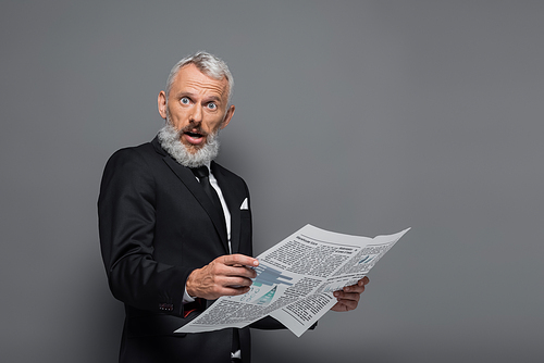 surprised middle aged businessman holding newspaper on grey