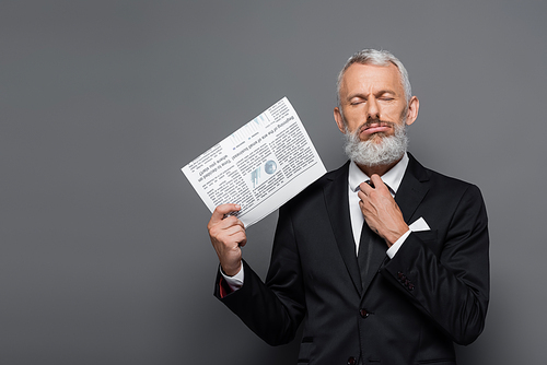 middle aged businessman adjusting tie and holding newspaper on grey