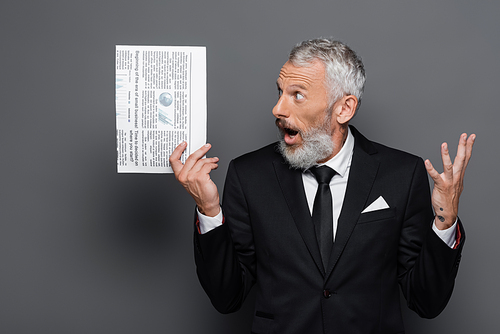 astonished middle aged businessman gesturing while holding newspaper on grey