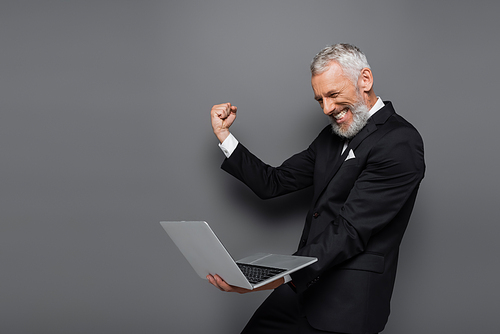 excited middle aged businessman in suit holding laptop on grey