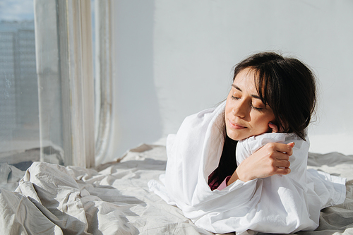 young armenian woman relaxing with closed eyes under white bedding